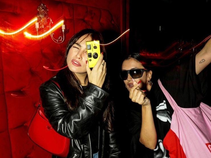Dos invitadas posando en una fiesta, una de ellas con una cámara Flasher amarilla